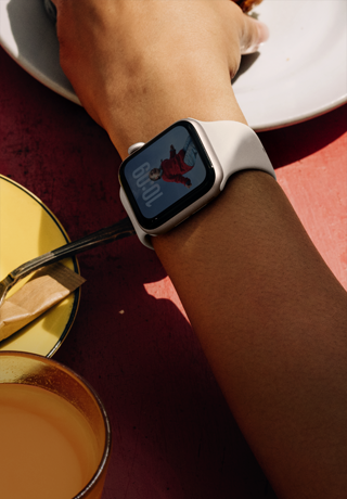 A person’s arm grabbing breakfast food, Apple Watch SE 3 on wrist, Starlight aluminium case, always-on display, portrait of a person on watch face, starlight Sport Band